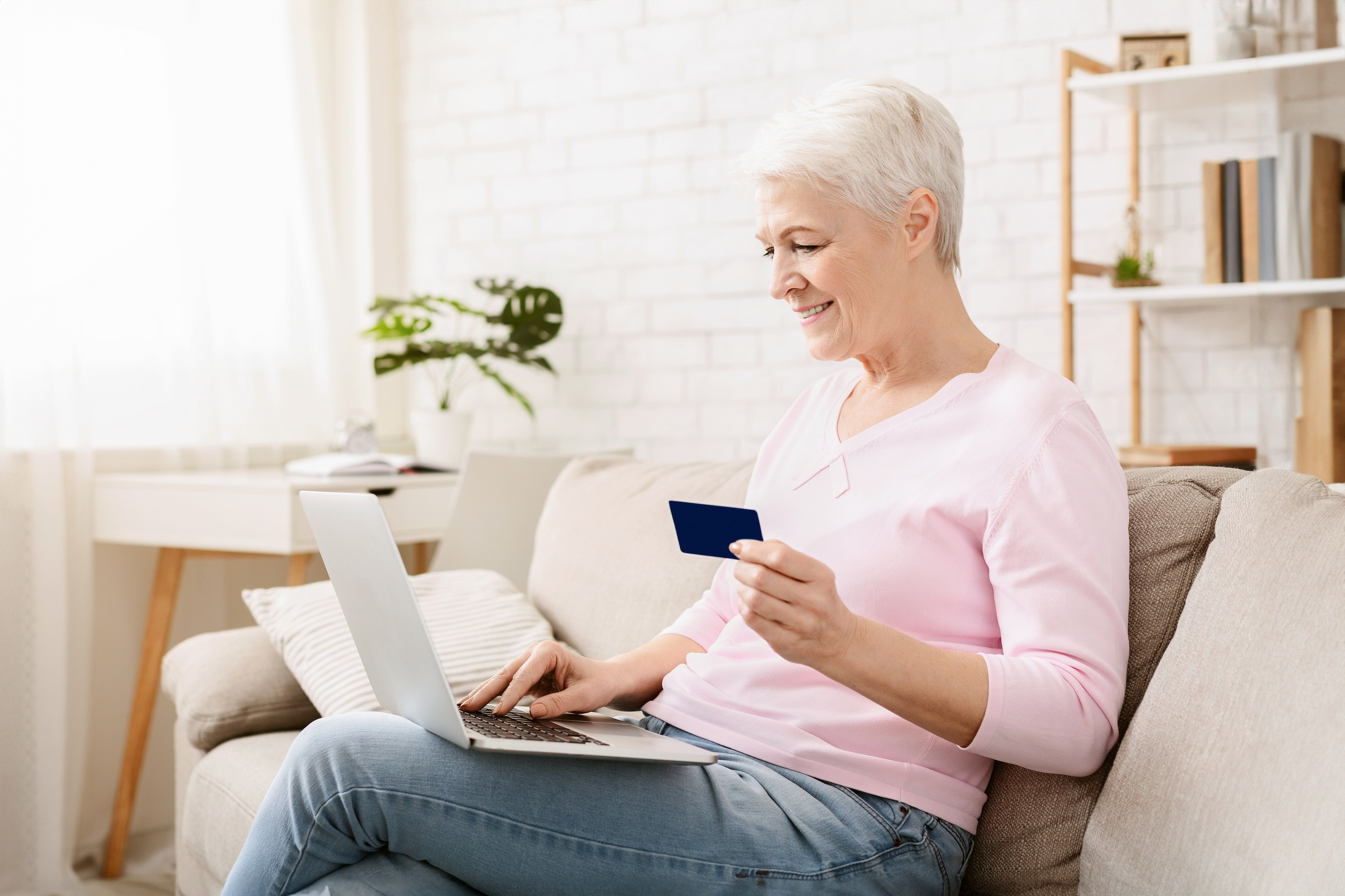 Seniorin sitzt mit Kreditkarte und Laptop auf dem Sofa