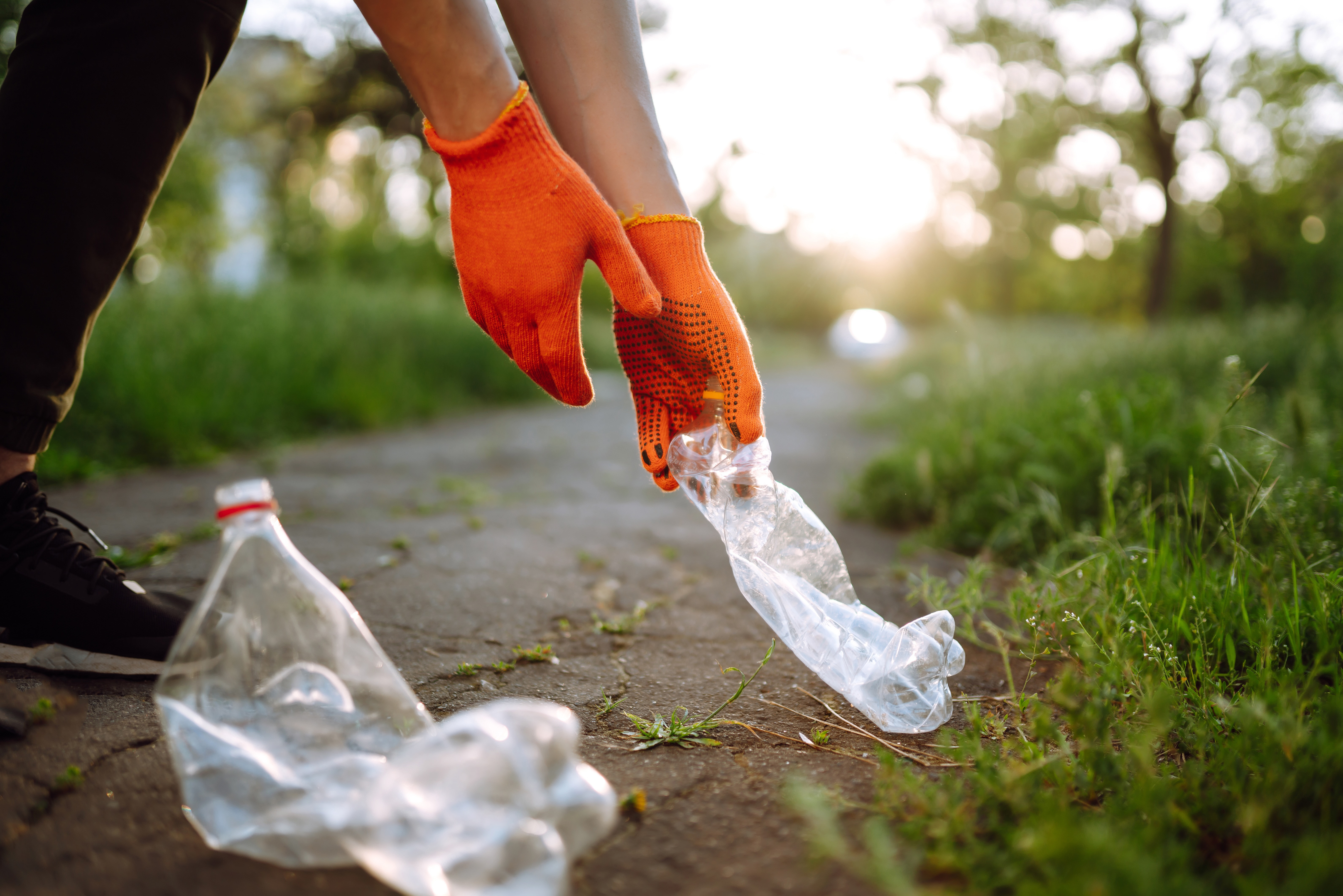 Person mit orangen Handschuhen sammelt leere Plastikflaschen ein