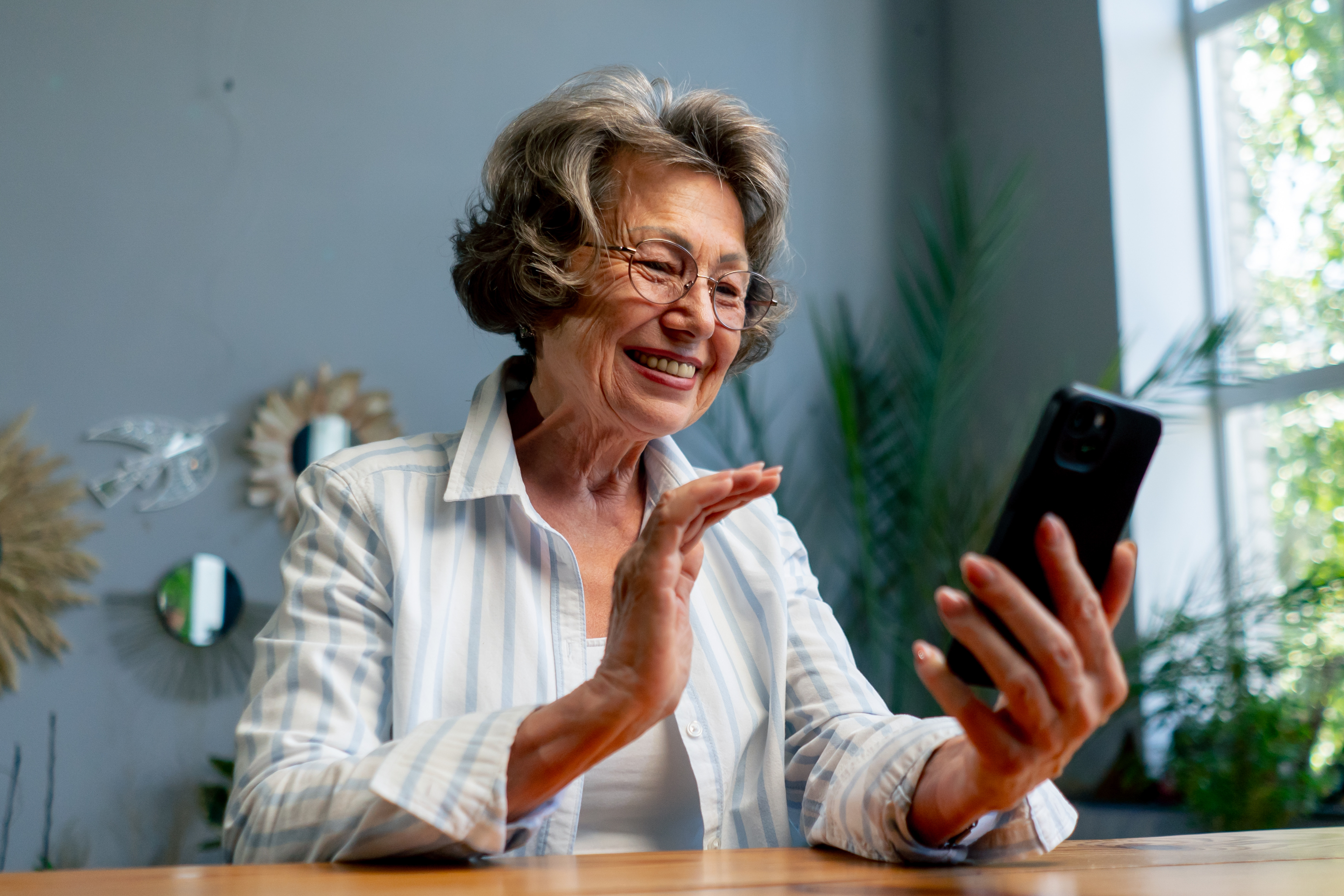 Ältere Frau lächelt und winkt in ihr Smartphone