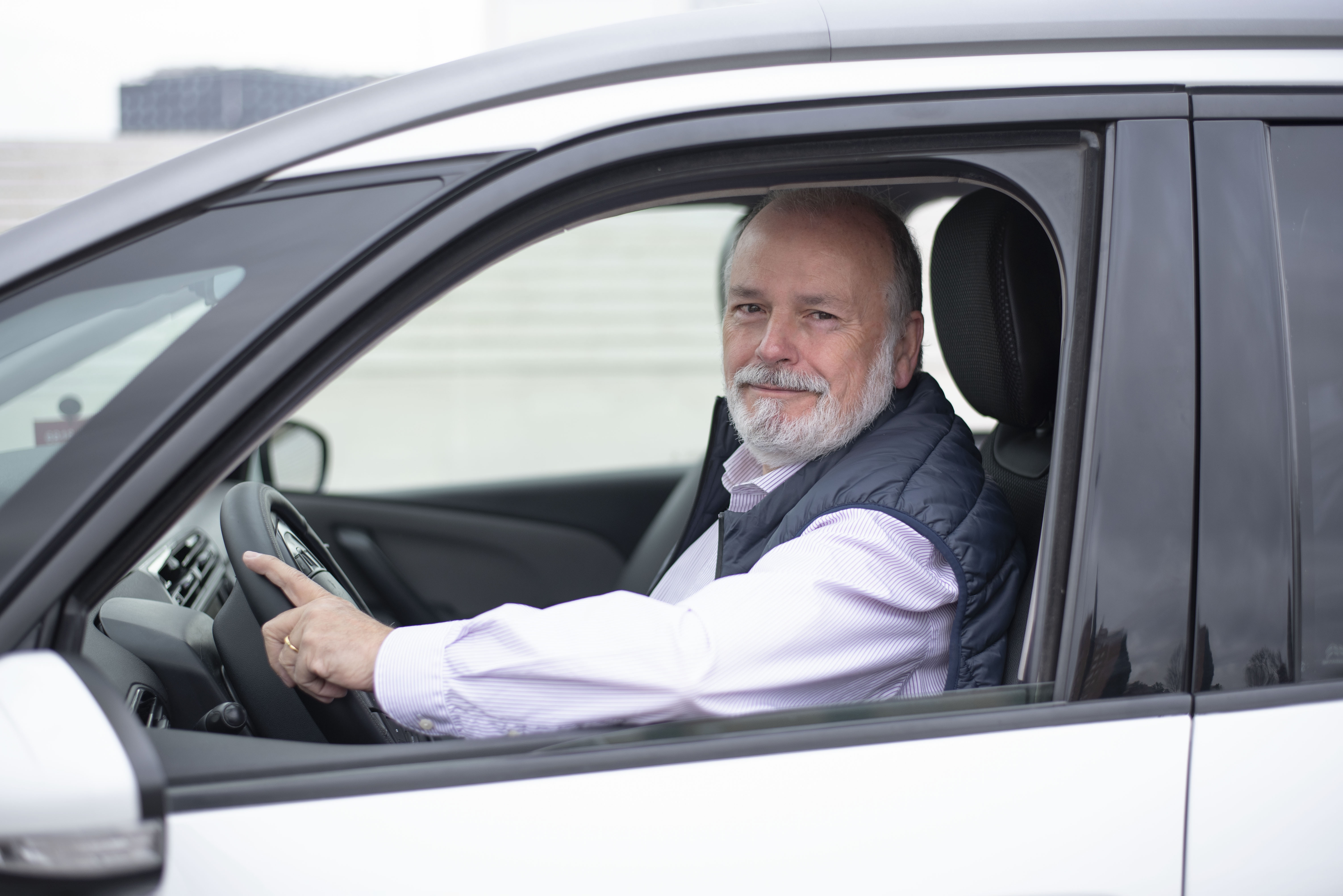 Senior sitzt am Steuer eines Autos und lächelt in die Kamera