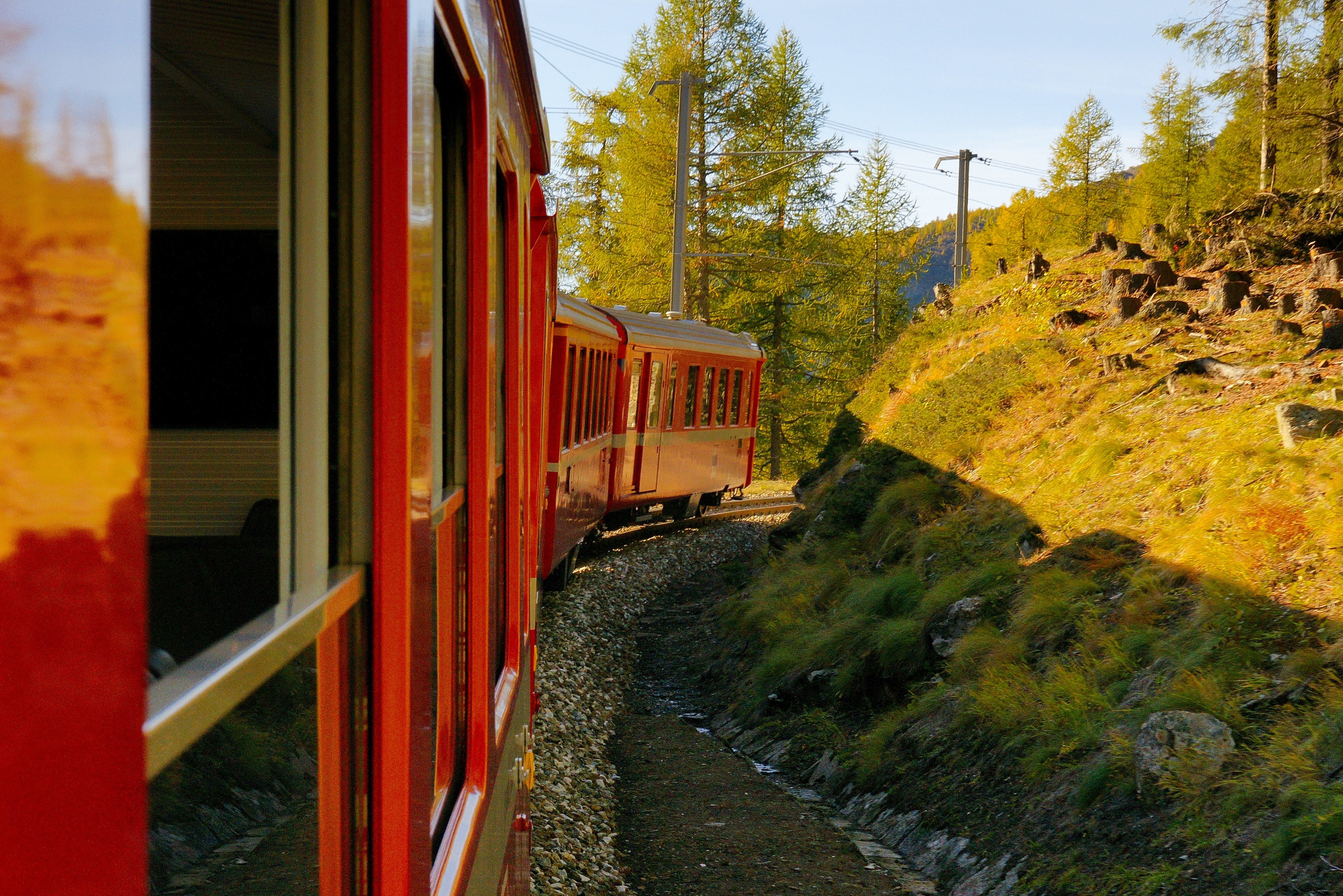 Roter Zug fährt eine Kurve an einem sonnigen Herbsttag