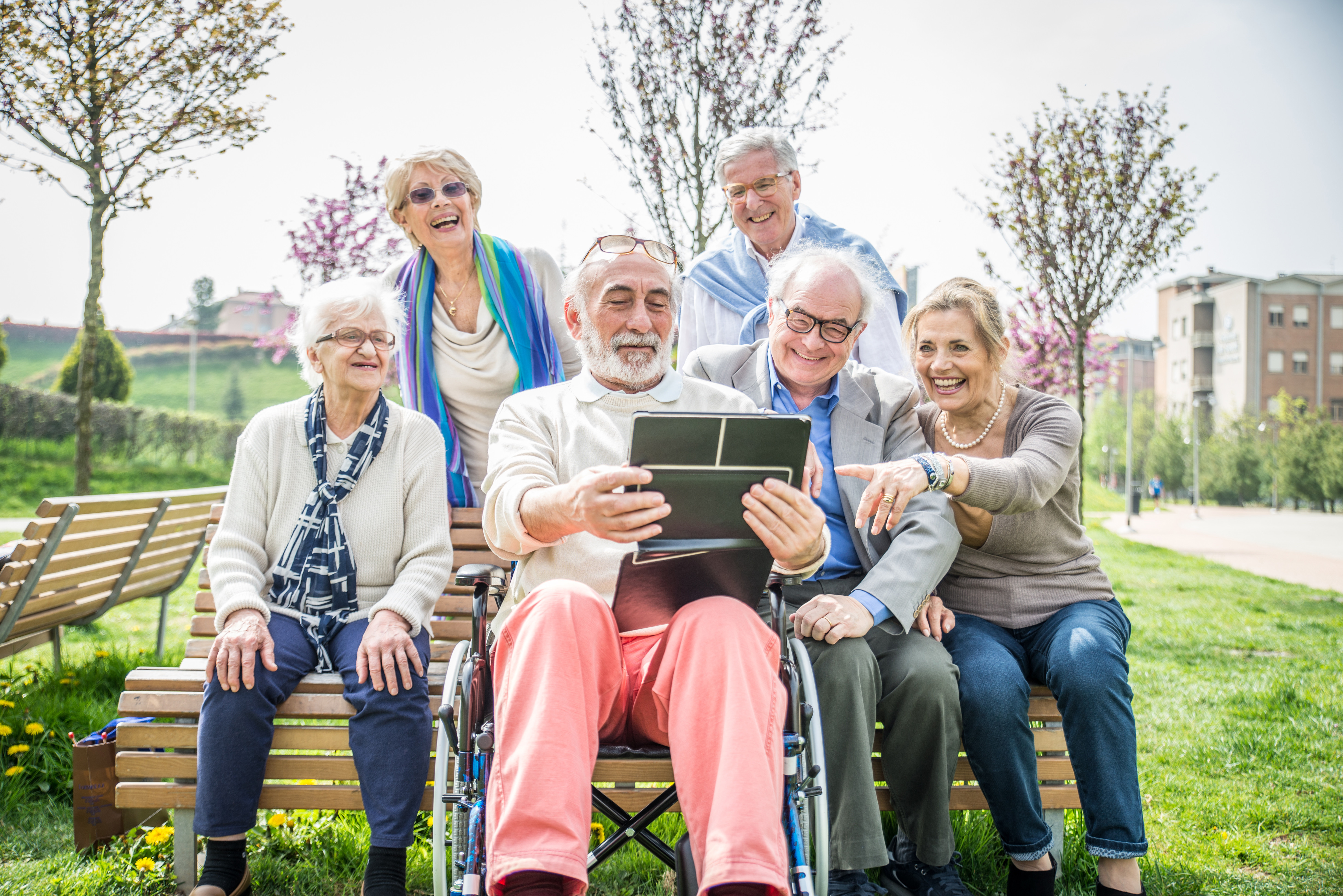 Gruppe von älteren Menschen sitzen auf Parkbank und schauen in ein Tablet
